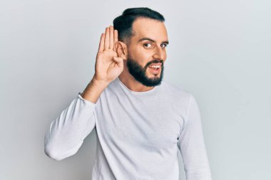 Sakallı genç bir adam, günlük beyaz gömlek giyiyor, kulağı kulağında gülümsüyor ve söylenti ya da dedikoduları dinliyor. Sağırlık kavramı. 