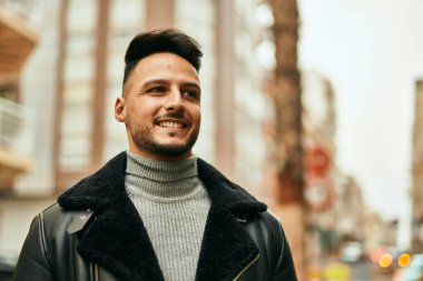 Genç Arap adam gülümsüyor, mutlu bir şekilde şehirde duruyor..