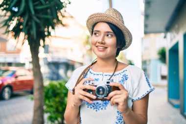 Tatildeki genç Latin turist kız şehirde klasik kamera kullanarak mutlu mesut gülümsüyor..