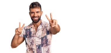 Yaz kıyafetleri giymiş genç İspanyol adam kameraya bakıp zafer işareti yapıyor. İki numara.. 