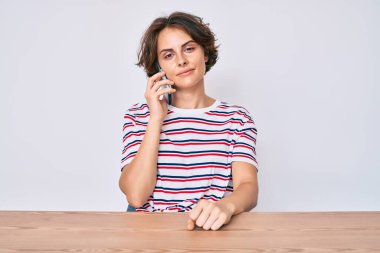 Genç İspanyol kadın akıllı telefonuyla konuşuyor. Masada oturuyor. Düşünme tavrı ve ayık yüz ifadesi. 