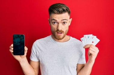 Genç kızıl saçlı adamın elinde akıllı telefon ve kumarhane kartı var. Şok olmuş suratında. Şüpheci ve alaycı görünüyor. 