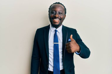 Yakışıklı, genç, takım elbiseli ve kravatlı mutlu ve pozitif gülümseyen, başparmağıyla mükemmel ve onay işareti yapan bir zenci. 