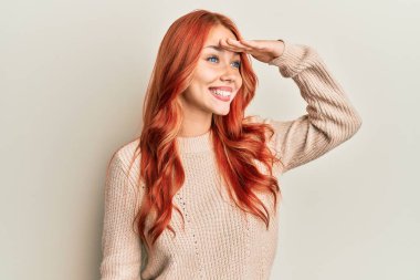 Genç, güzel, kızıl saçlı, sıradan bir kazak giyen mutlu ve gülümseyerek başını kaldırmış uzaklara bakan bir kadın. arama kavramı. 