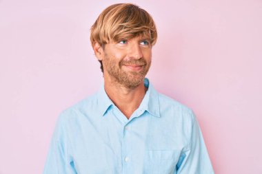 Sıradan kıyafetler giyen genç sarışın adam, rahat bir görünüm takınıyor, doğal bir yüz ve kendine güvenen bir gülümsemeyle poz veriyor.. 