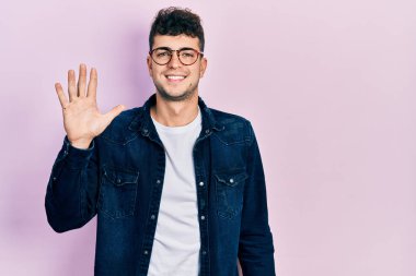 Gündelik kıyafetler giyen ve gözlük takan genç İspanyol adam beş numarayı gösterip işaret ederken kendinden emin ve mutlu gülümsüyor.. 