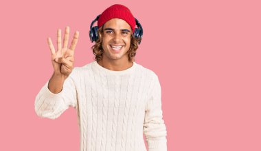 Genç İspanyol adam kulaklık kullanarak müzik dinliyor. Dört numaralı parmaklarıyla işaret ediyor ve gülümsüyor. Kendinden emin ve mutlu.. 