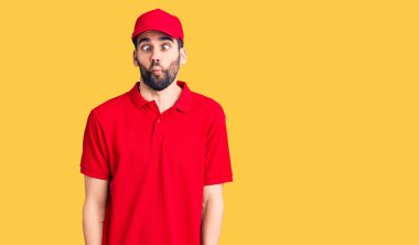 Sakallı, teslimat üniformalı, dudakları balık suratlı, çılgın ve komik bir jest yapan yakışıklı bir genç. Komik ifade. 