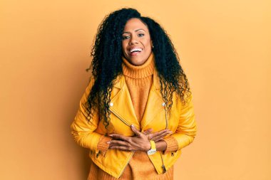 Orta yaşlı Afro-Amerikalı kadın yün kazak ve deri ceket giyiyor. Gülüyor ve sırıtıyor.. 