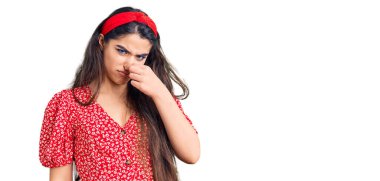 Brunette teenager girl wearing summer dress smelling something stinky and disgusting, intolerable smell, holding breath with fingers on nose. bad smell 