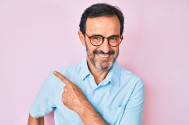 Orta yaşlı İspanyol bir adam, günlük kıyafetler ve gözlük takıyor. Gülümsüyor, gülümsüyor, elleri ve parmakları yana bakıyor. 