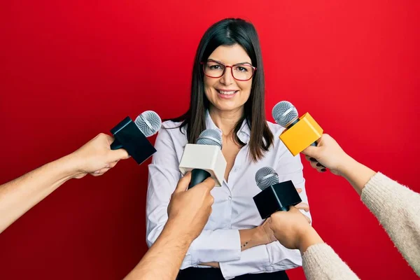 Young hispanic woman being interviewed for journalist hands with microphone happy face smiling with crossed arms looking at the camera. positive person.