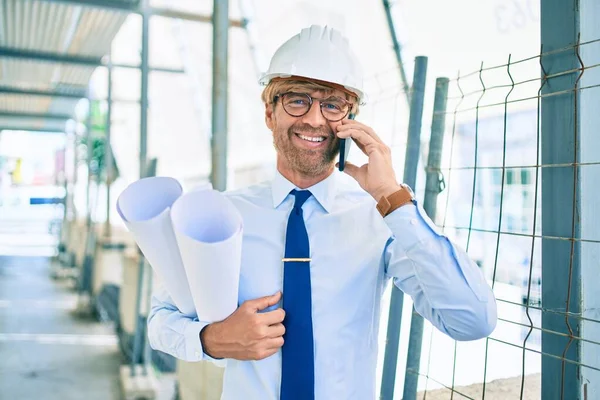 電話で話している建物のプロジェクトの外に立っているハードハットを身に着けているビジネスアーキテクトの男 — ストック写真