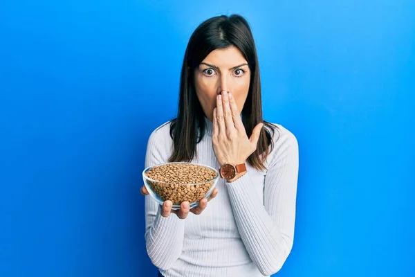 若いヒスパニック系の女性の手で口をカバーし ボウルレンズ豆を保持ショックを受け ミスを恐れている 驚きの表情 — ストック写真