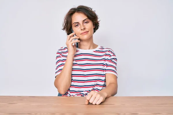 Mujer Hispana Joven Hablando Teléfono Inteligente Sentada Mesa Pensando Actitud —  Fotos de Stock