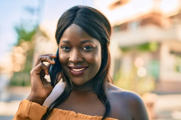 若いアフリカ系アメリカ人女性が笑顔で市内のスマートフォンで話しています — ストック写真