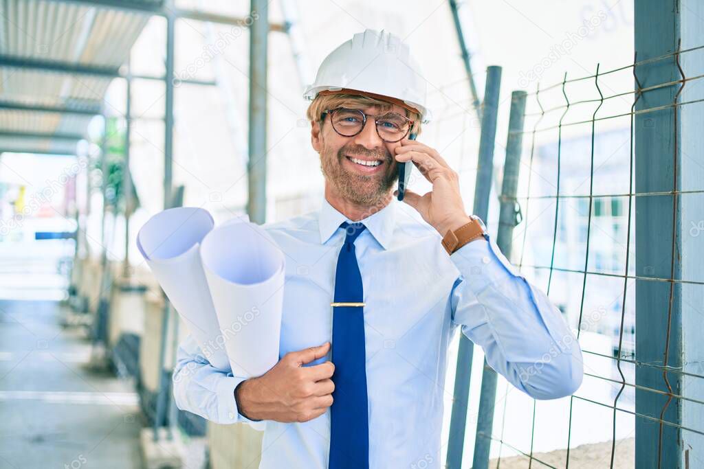 Business architect man wearing hardhat standing outdoors of a building project speaking on the phone
