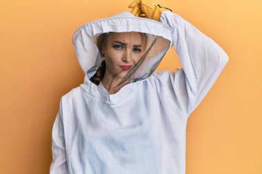 Koruyucu arıcı üniforması giyen güzel sarışın beyaz kadın soru sormayı merak ediyor. Şüpheyle kararsız, kafa kafaya düşünerek. Düşünceli kavram. 