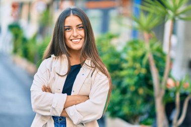 Kollarını kavuşturmuş genç İspanyol kız şehirde mutlu bir şekilde gülümsüyor..