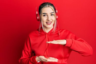 Spor kıyafetleri giyen ve kulaklık takan genç modern bir kız. Büyük ve büyük beden işareti olan el hareketleriyle işaret ediyor. Ölçü sembolü. Kameraya bakıp gülümsüyor. ölçüm kavramı. 