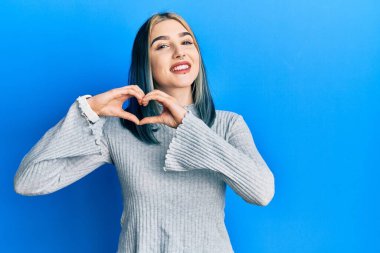 Genç, modern bir kız, sıradan bir süveter giyer, aşka gülümser, elleriyle kalp sembolü çizer. romantik kavram. 