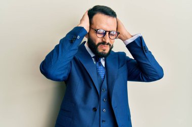 Sakallı, takım elbiseli, kravatlı, baş ağrısı çeken çaresiz ve stresli bir genç adam. Ağrı ve migren yüzünden. Eller başının üstünde.. 