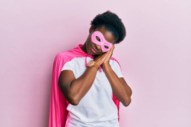 Genç Afro-Amerikalı kız süper kahraman maskesi ve pelerin giyip uyuyordu. Yorgun düşler kurup, elleri ile poz verirken gözleri kapalıydı.. 