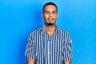 Gündelik kıyafetler giyen genç Afro-Amerikan adam yüzünde ciddi bir ifadeyle rahatlamış. Basit ve doğal bir şekilde kameraya bakıyorsun.. 