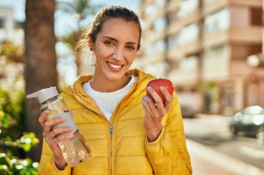 Genç İspanyol kız şehirde bir şişe su içip elma yiyor..