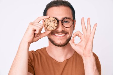 Kurabiye tutan genç yakışıklı adam parmaklarıyla imza atıyor, gülümseyerek mükemmel bir sembol oluşturuyor. 