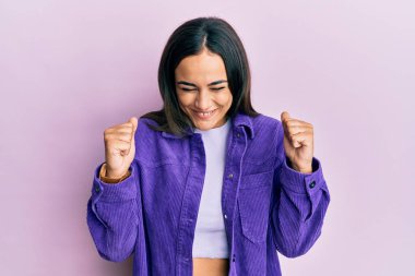 Gündelik kıyafetler giyen genç esmer kadın başarı için heyecanlı kolları havada ve gözleri kapalı zaferi kutlarken gülümsüyor. Kazanan konsept. 