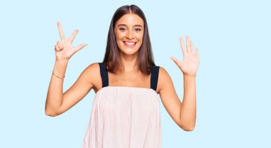 Genç İspanyol kadın gündelik kıyafetler giyer ve sekiz numaralı parmaklarıyla gülümseyerek mutlu ve kendinden emin bir şekilde işaret eder.. 