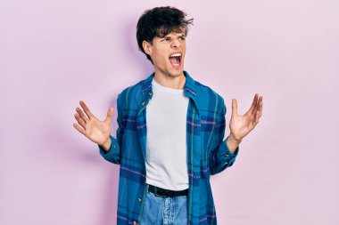 Yakışıklı hippi genç adam gündelik beyaz tişört ve klasik gömlek giyiyor. Deli gibi bağırıyor, agresif bir ifadeyle bağırıyor ve kollarını kaldırıyor. hüsran kavramı. 