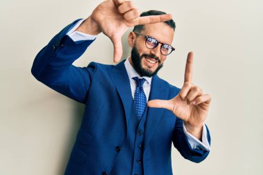 Sakallı, takım elbiseli, kravatlı, gülümseyen, elleri ve parmakları gülen yüzlü genç bir adam. yaratıcılık ve fotoğrafçılık kavramı. 