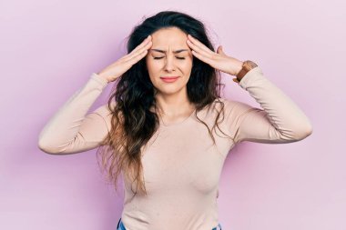 Elleri başının üstünde, günlük kıyafetler giyen genç İspanyol kadın, stres yüzünden baş ağrısı çekiyor. migren ağrısı. 