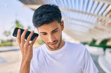 Genç Latin adam gülümsüyor. Şehirde akıllı telefon kullanarak mutlu bir sesli mesaj dinliyor..