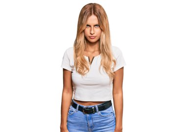 Gündelik beyaz tişört giyen, kuşkucu ve gergin, güzel sarışın genç bir kadın sorun yüzünden üzgün. negatif kişi. 
