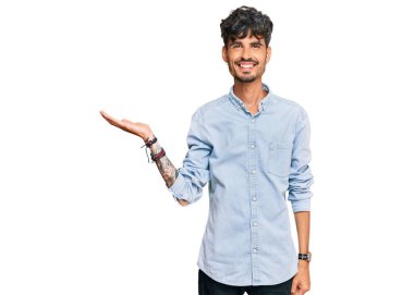 Gündelik kıyafetler giyen genç İspanyol adam neşeli bir şekilde gülümsüyor ve avuç içi kameraya bakıyor.. 