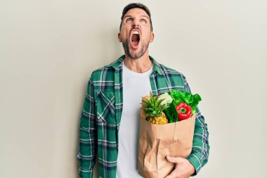 Sakallı yakışıklı bir adam elinde alışveriş torbalarıyla öfkeli ve kızgın çığlıklar atıyor öfkeyle bağırıyor. öfke ve agresif konsept. 