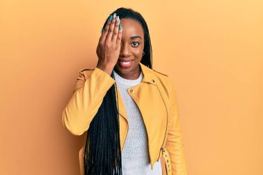 Genç, Afro-Amerikan bir kadın. Günlük ceket giyiyor. Bir gözünü eliyle kapatıyor.. 