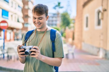 Beyaz tenli genç turist şehirde klasik kamera kullanarak mutlu bir şekilde gülümsüyor..