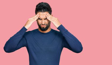 Sakallı genç adam günlük mavi süveter giyiyor. Baş ağrısı ve stres yüzünden acı çekiyor. Ağrı ve migren yüzünden. Eller başının üstünde.. 