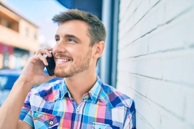 Genç beyaz adam gülümsüyor. Şehirdeki akıllı telefondan konuşuyor..