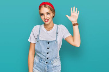 Gündelik giysiler giyen genç beyaz kız beş numarayı gösterip işaret ederken kendinden emin ve mutlu bir şekilde gülümsüyor.. 