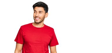 Young handsome man wearing casual red tshirt smiling looking to the side and staring away thinking. 