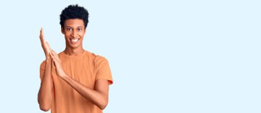 Genç Afro-Amerikan adam günlük giysiler içinde alkışlıyor ve mutlu ve neşeli alkışlıyor, gururla gülümsüyor. 