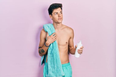 Genç İspanyol adam mayo giyiyor ve elinde güneş kremi tutuyor. Gülümsüyor ve başka tarafa bakıyor.. 