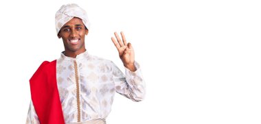 Gelenek giyinmiş Afrikalı yakışıklı bir adam Sherwani sari giysileri giyiyor ve üç numaralı parmaklarıyla işaret ederken kendinden emin ve mutlu gülümsüyor.. 