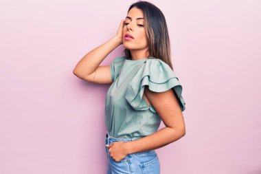 Genç, güzel, esmer, günlük kıyafetler giyen bir kadın izole edilmiş pembe arka planda dikiliyor.