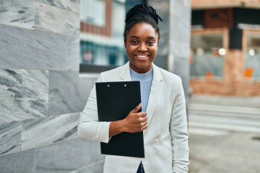Genç Afrikalı Amerikalı iş kadını, şehirde elinde bir panoyla mutlu bir şekilde gülümsüyor..